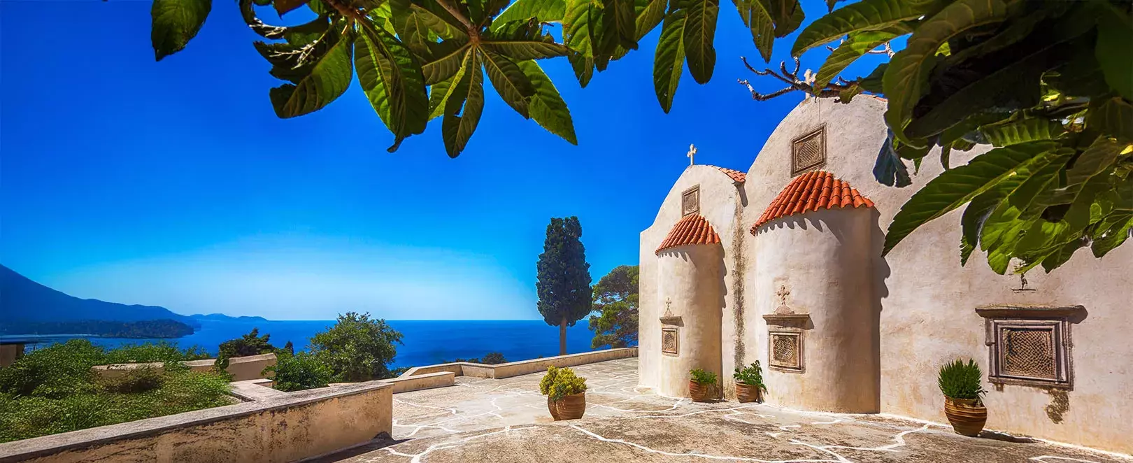Chapelle blanche surplombant la mer en Crète, vue panoramique sur la côte et le bleu de la mer Égée par temps clair.