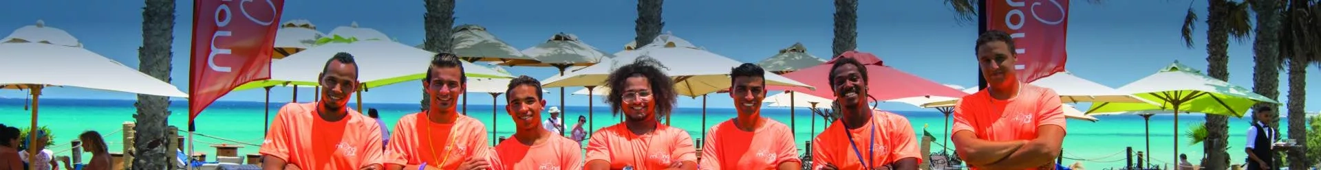 Équipe d'animateurs posant devant des bannières Mondi Club sur la plage