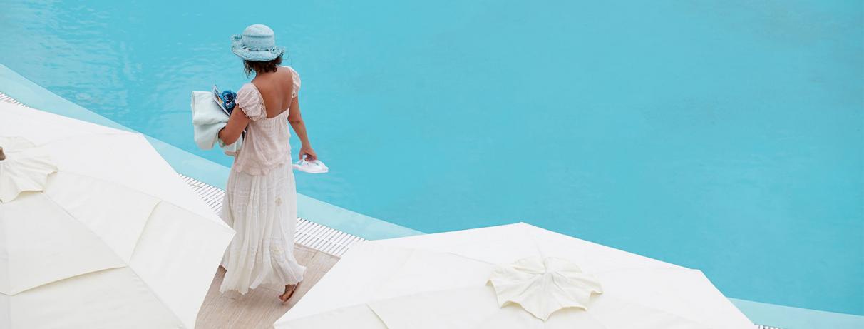 femme avec robe et chapeau blancs se promenant au bord de la piscine
