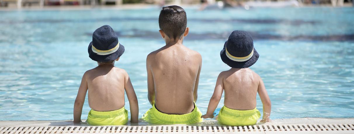 3 enfants de dos assis au bord de la piscine