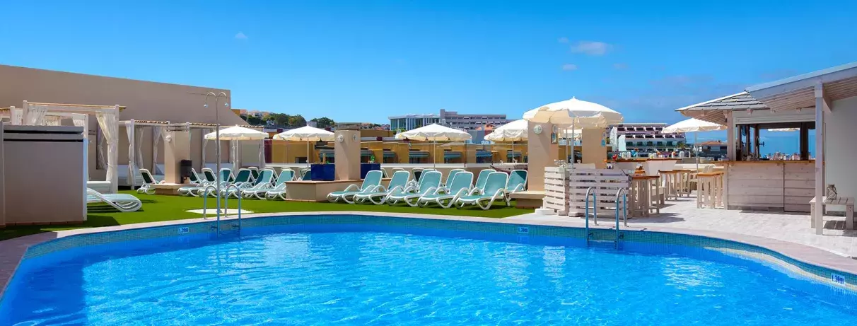 Une piscine d'un bleu éclatant entourée de parasols blancs et de bâtiments élégants sous un ciel radieux.