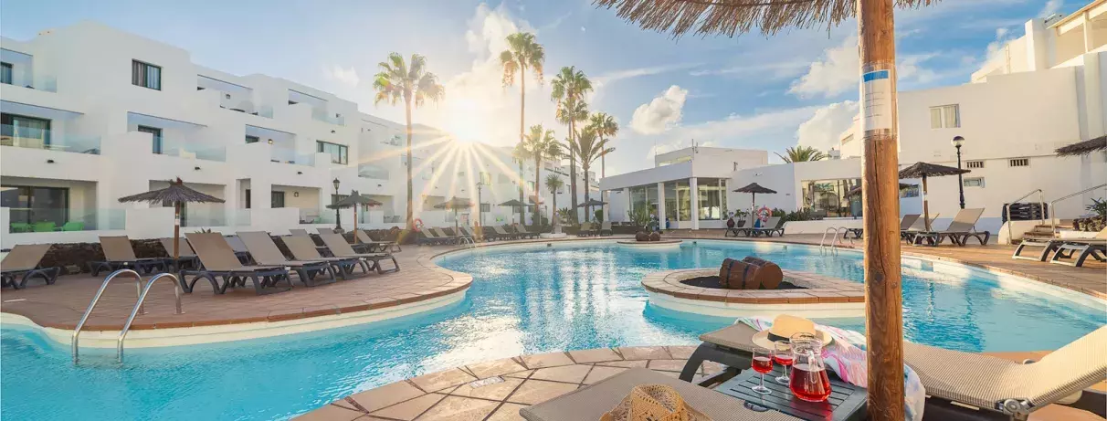vue sur la piscine  avec transats et palmiers et coucher de soleil