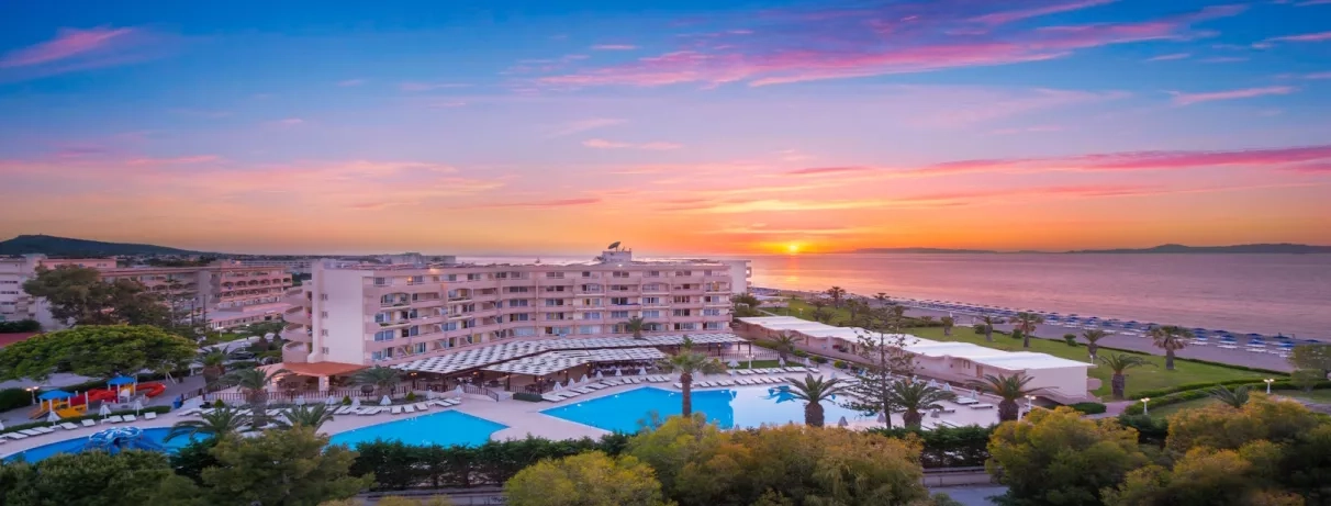 Vue d'ensemble bâtiment de l'hôtel avec 3 piscines, terrasse restaurant, transats, parasols, plage, coucher de soleil