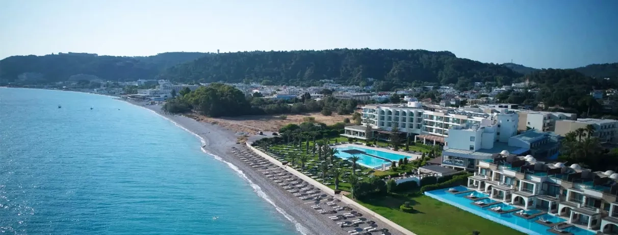 vue d'ensemble plage, transats et parasols paillote, jardin, végétation, palmiers, chambres avec piscines