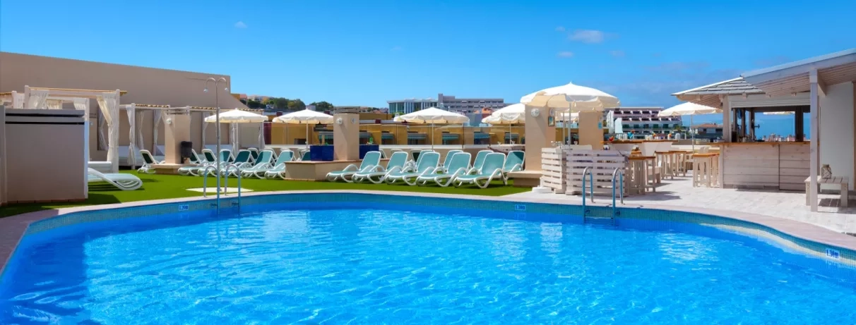 Une piscine d'un bleu éclatant entourée de parasols blancs et de bâtiments élégants sous un ciel radieux.