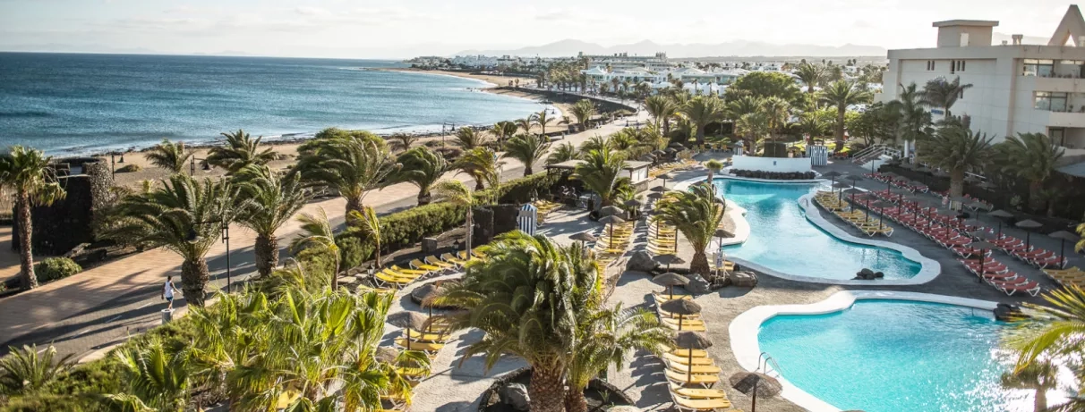 Une vue en hauteur montrant une longue piscine qui s'étend vers une plage, bordée par l'océan bleu.
