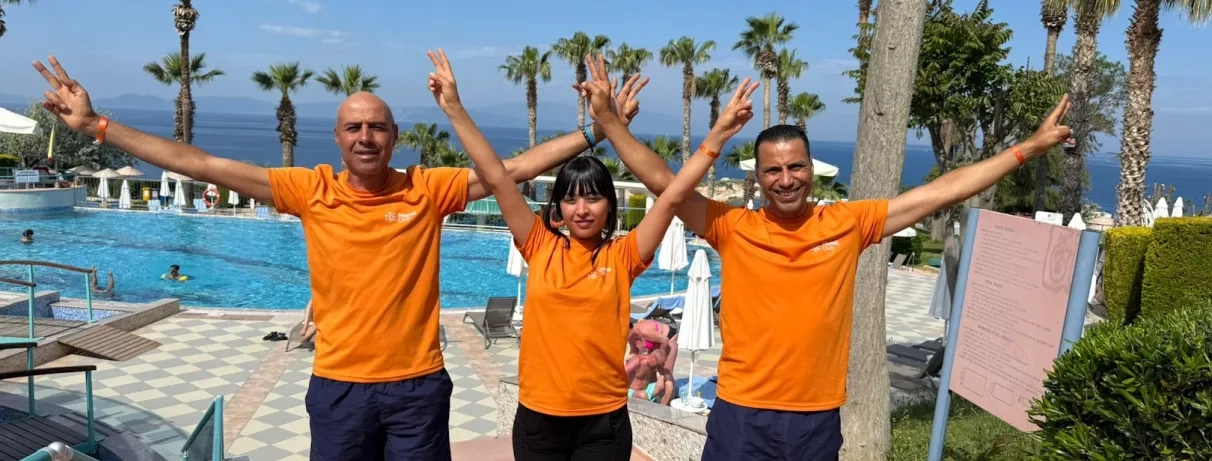 Trois animateurs, posent les bras levés devant une piscine en plein air.