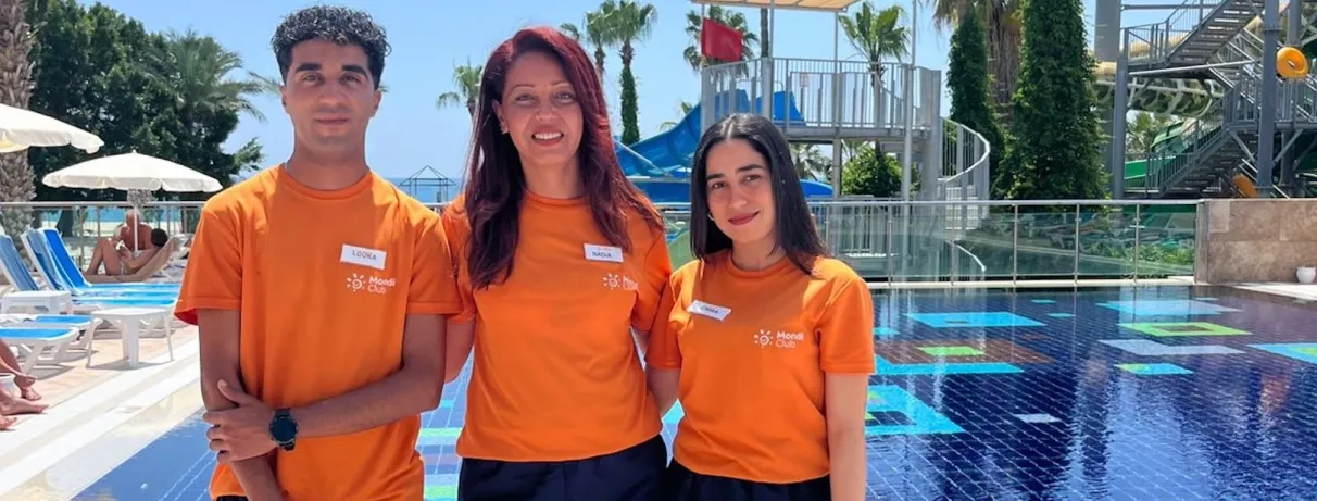Trois animateurs posent côte à côte devant une piscine extérieure ensoleillée.