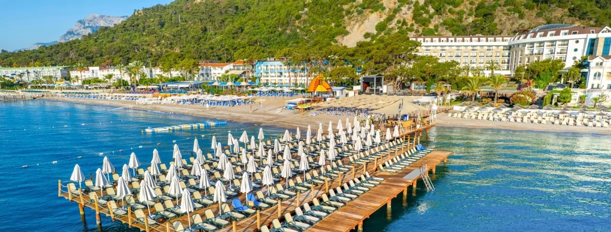 Un ponton en bois avec des transats et des parasols au milieu de la mer rejoignant la plage.