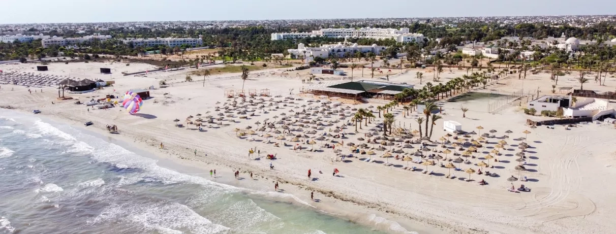 Une immense plage de sable fin bordée de parasols en paille, avec ses espaces dédiés aux sports nautiques.