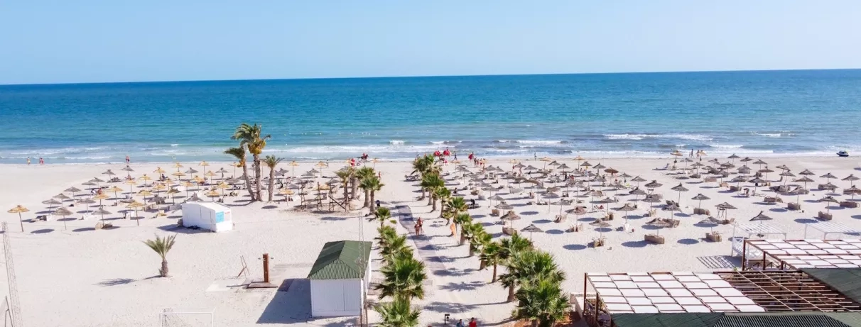 Une vaste étendue de sable blanc parsemée de parasols traditionnels, face à une mer turquoise.