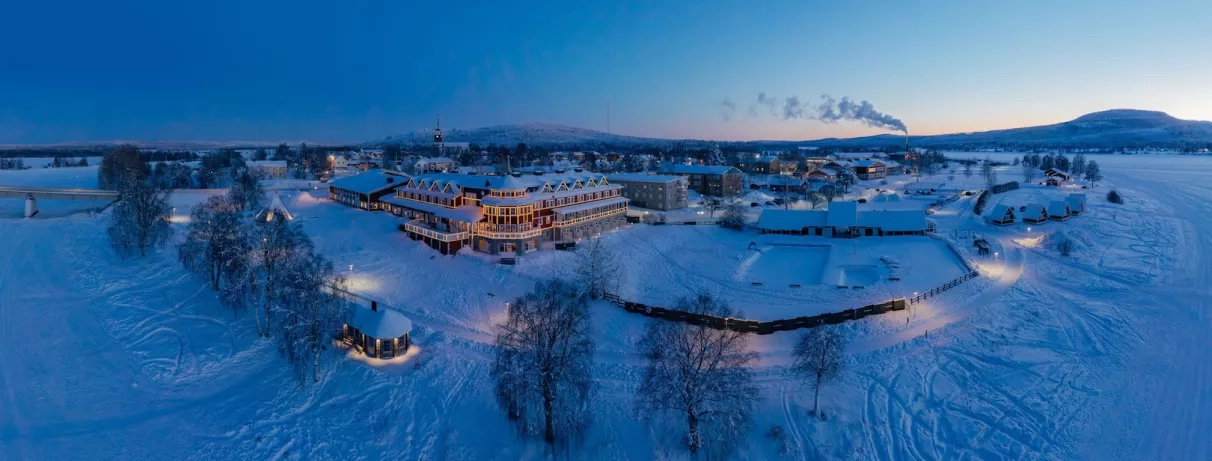 Vue panoramique enneigée de l'hôtel Grand Arctic Resort illuminé au crépuscule en Laponie suédoise.