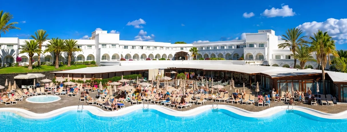 Une vue panoramique d'une grande piscine, bordée de transats devant l'hôtel.