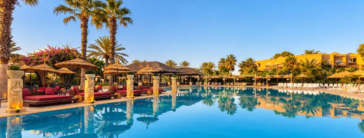 Grande piscine entourée de palmiers, transats confortables et ambiance ensoleillée