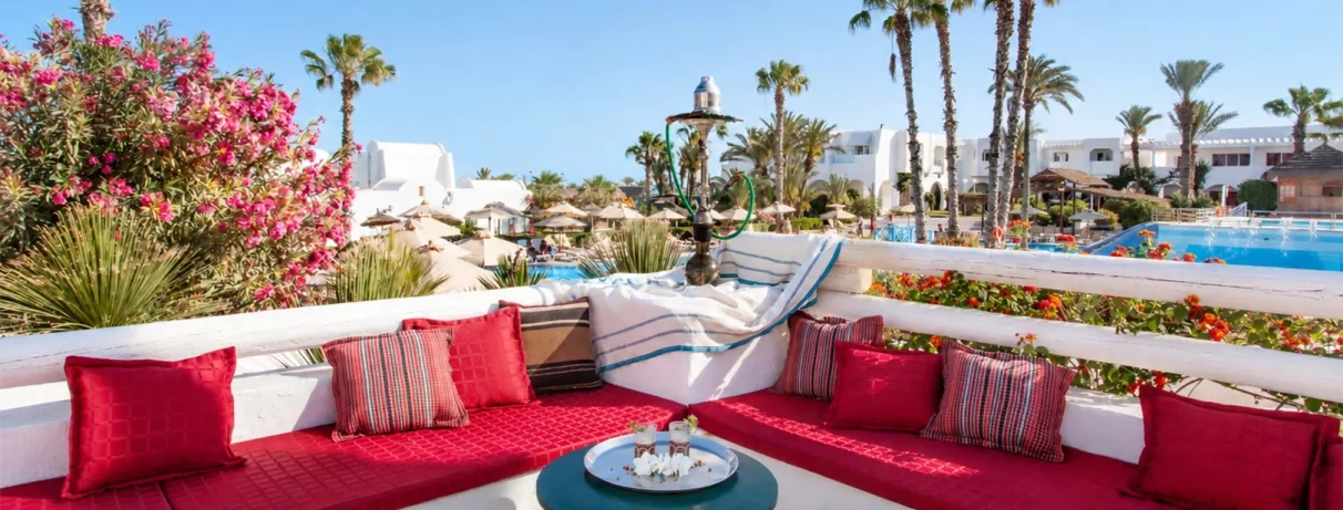 Espace détente en terrasse du Mondi Club Aladin Djerba avec banquette rouge, chicha traditionnelle et vue sur la piscine et les palmiers.