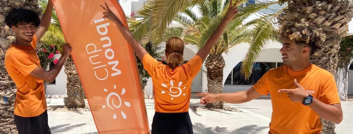 Équipe d'animateurs du Mondi Club Aladin Djerba vêtus d'oranges posant joyeusement devant la flamme de la marque.