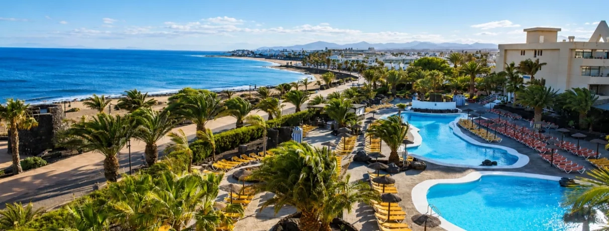 Une vue en hauteur montrant une longue piscine qui s'étend vers une plage, bordée par l'océan bleu.
