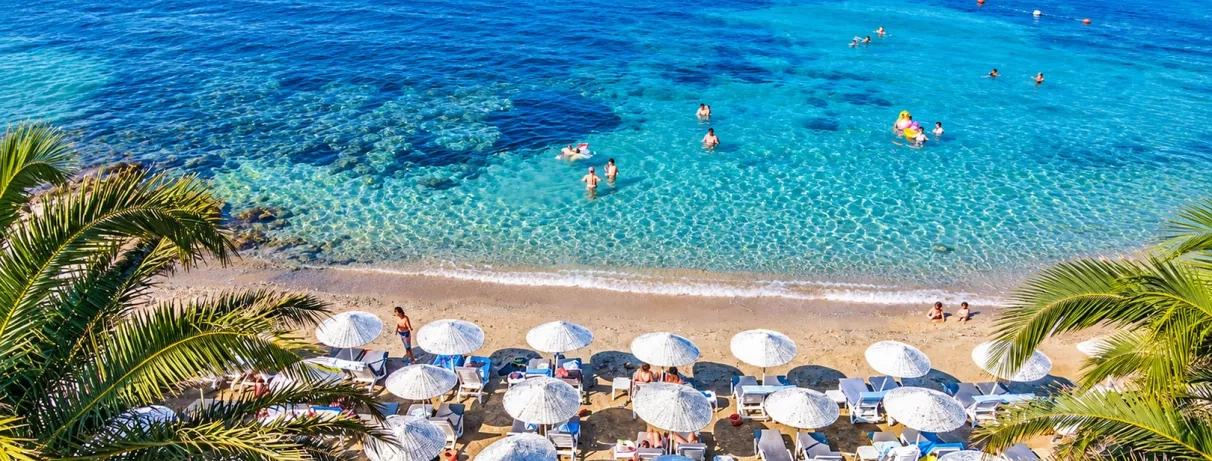 Une plage ensoleillée avec de nombreux parasols blancs alignés au bord de l'eau.