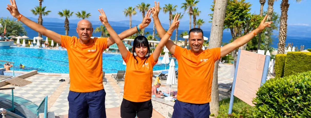 Trois animateurs, posent les bras levés devant une piscine en plein air.