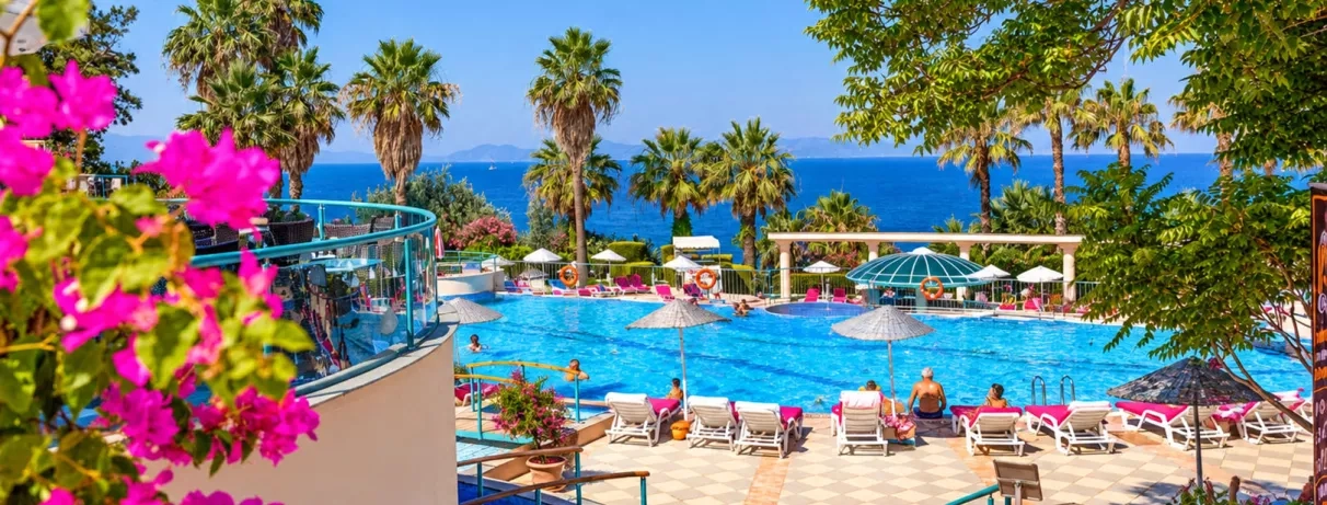 Une piscine animée sous un ciel bleu, entourée de parasols et de palmiers.