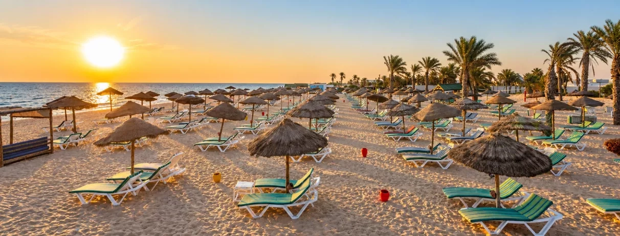 Plage privée de sable fin avec parasols en paille au coucher du soleil au Welcome Meridiana Djerba