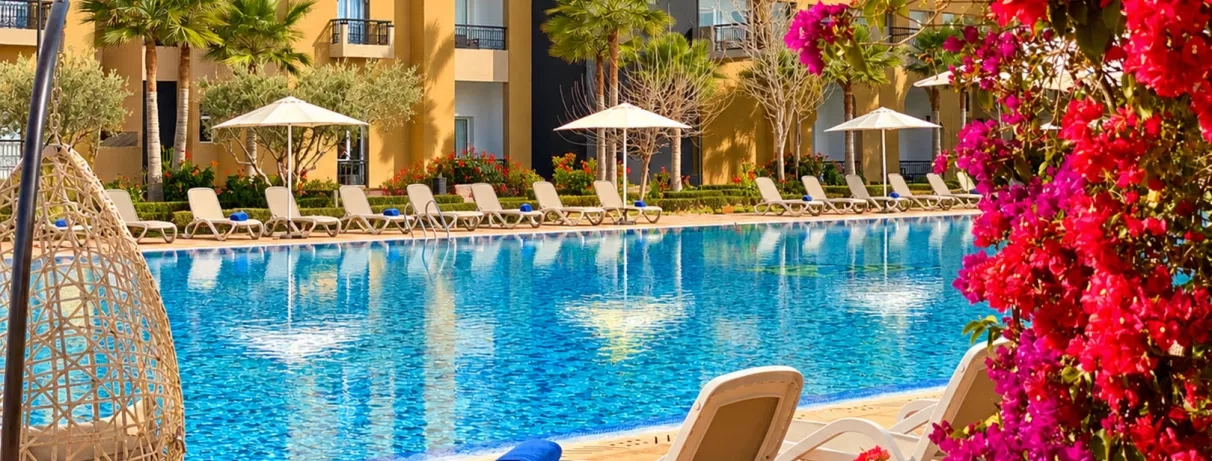 piscine en premier plan avec les transats juste derrière et au fond le bâtiment des chambres