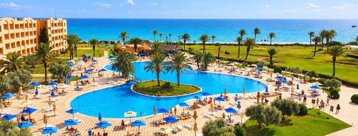 Grande piscine lagune entourée de palmiers et transats au club de vacances Nour Palace Mahdia en Tunisie.