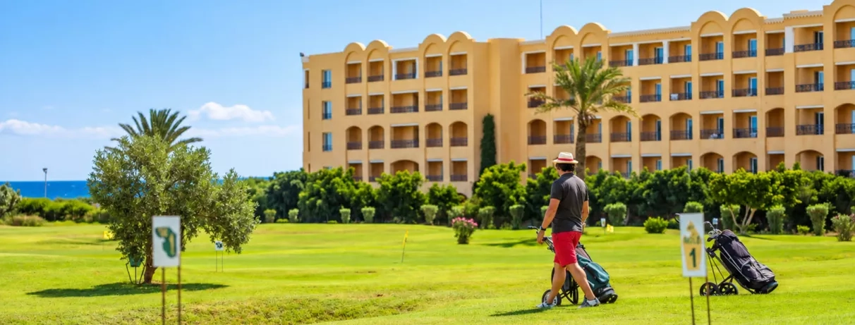 Touriste jouant au golf sur le terrain verdoyant devant les bâtiments de l'hôtel Nour Palace à Mahdia.