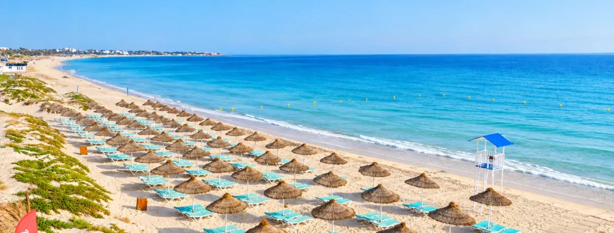 Plage privée de sable fin et parasols en paillote au Mondi Club One Resort Jockey à Monastir, Tunisie