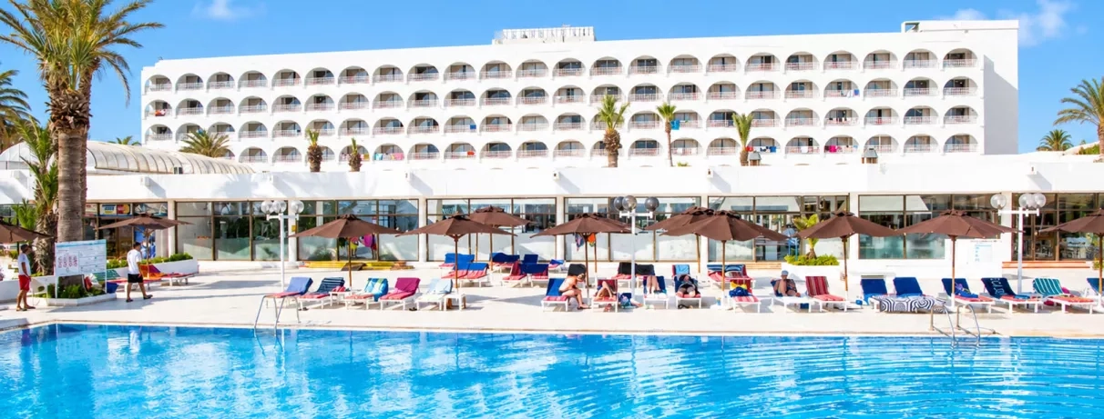 Grande piscine extérieure et transats devant la façade de l'hôtel Mondi Club One Resort Jockey Monastir