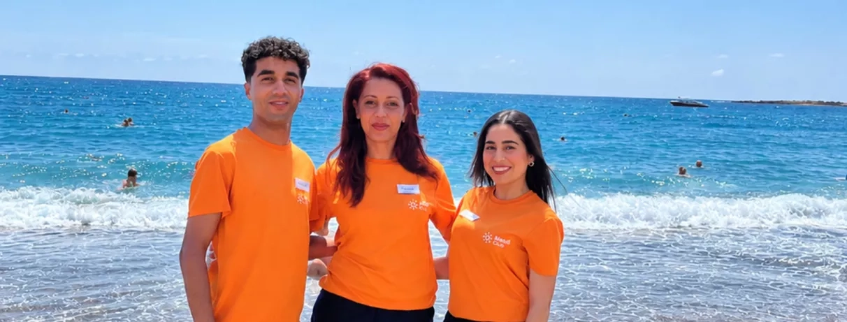 Trois animateurs posent côte à côte devant une piscine extérieure ensoleillée.