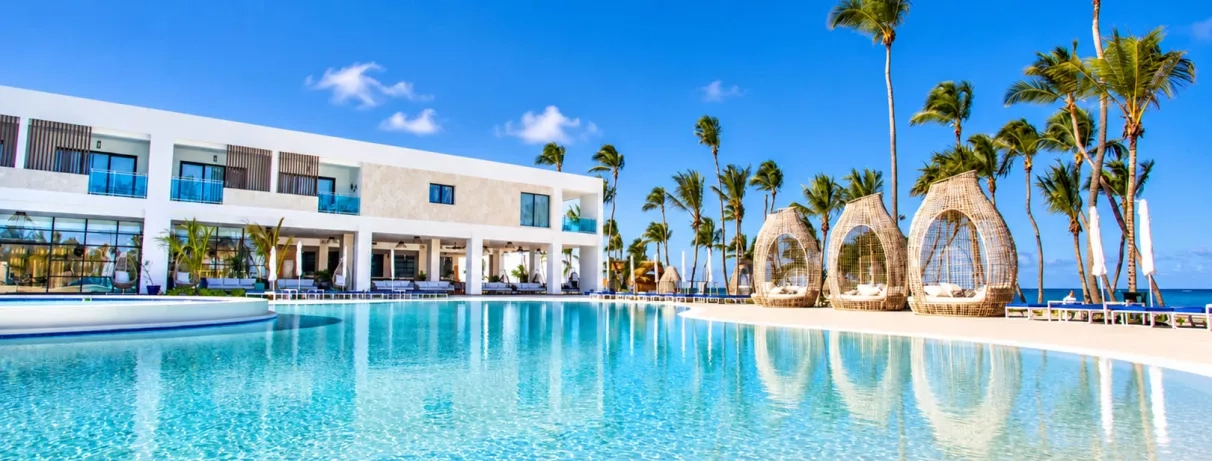 piscine, banquettes, palmiers, transats, ciel bleu, végétation luxuriante