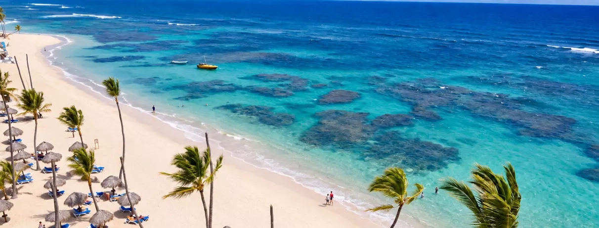 plage de sable blanc, eau turquoise, palmiers, transats bleus et parasols