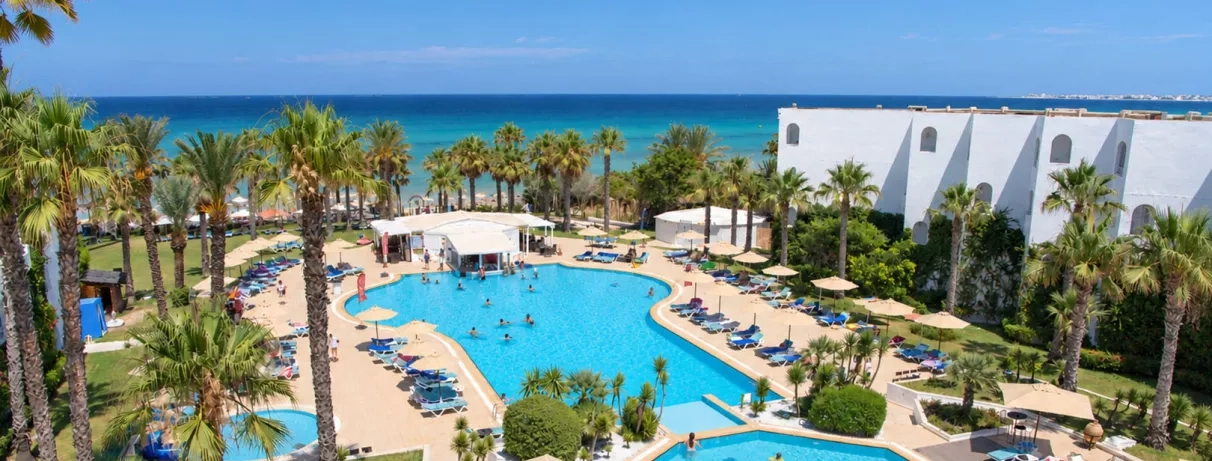 Vue aérienne de la grande piscine extérieure du Mondi Club Thalassa Mahdia entourée de palmiers avec la mer Méditerranée en arrière-plan à Mahdia en Tunisie.