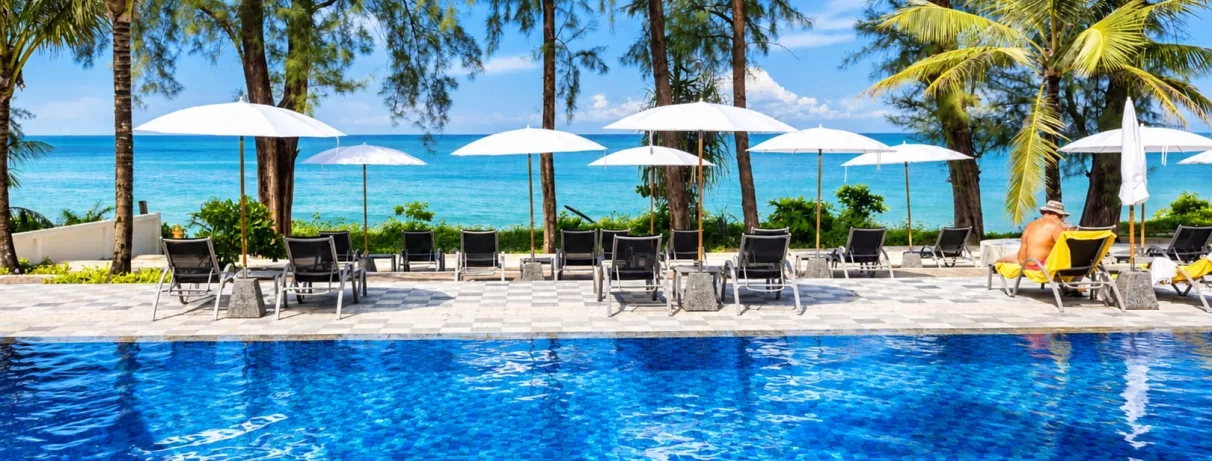 Vue d'une piscine bordée de palmiers avec des parasols blancs, des transats.