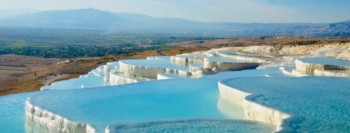 Des terrasses de calcaire blanc remplies d'eaux thermales turquoise, surplombant la vallée.