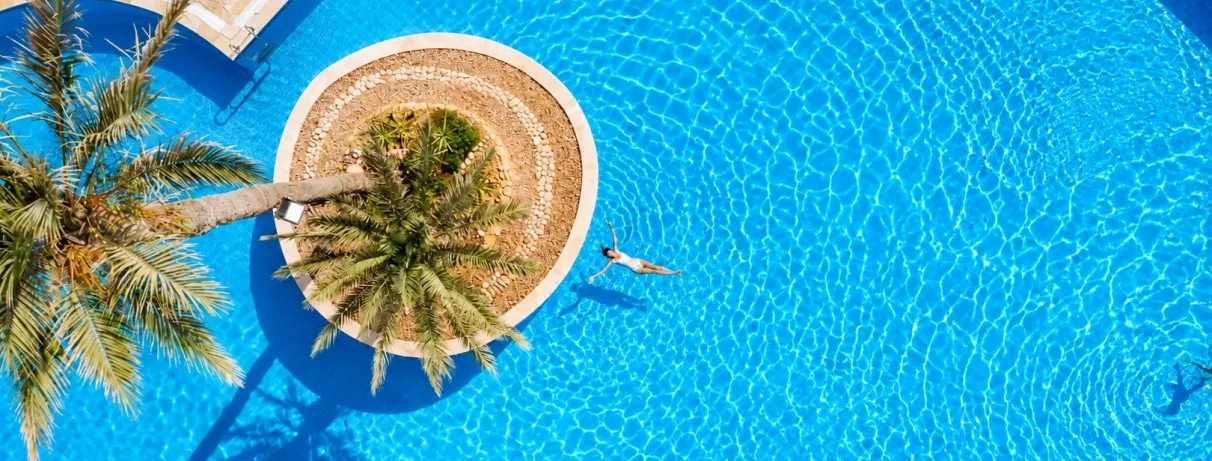 Femme nageant dans l'eau bleue d'une piscine circulaire avec palmier central au Djerba Golf.