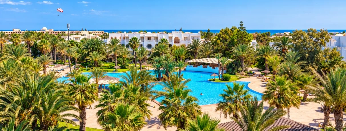 Vue panoramique sur la piscine lagon et les jardins tropicaux du Djerba Resort sous le soleil.