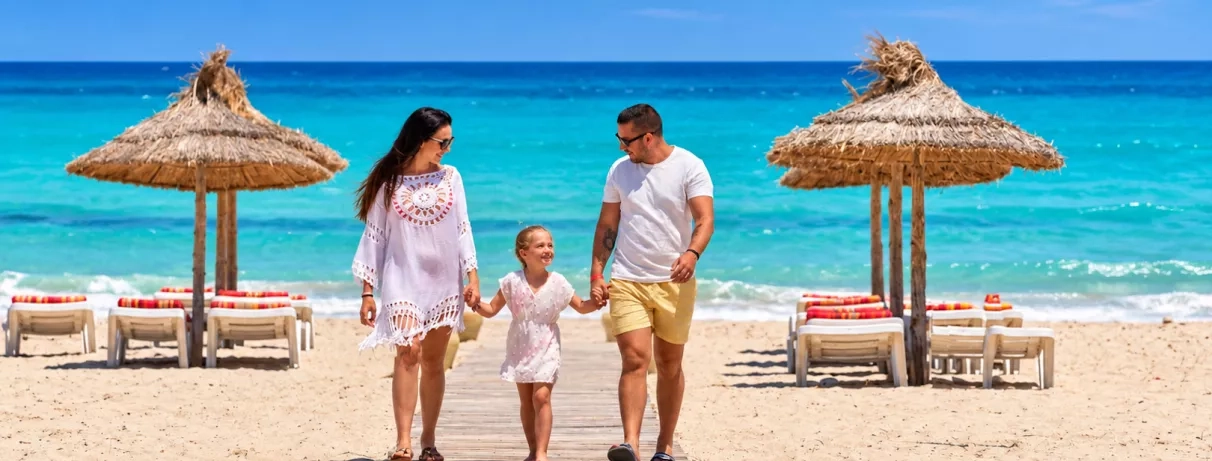 Famille marchant sur une plage de sable fin bordée de parasols typiques aux Quatre Saisons à Djerba.