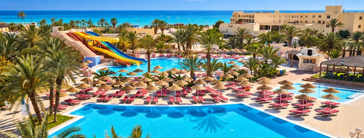 Parc aquatique avec toboggans colorés, piscines et palmiers au complexe hôtelier Quatre Saisons à Djerba, Tunisie.