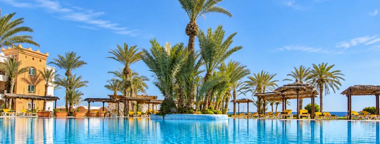 Vue de la piscine bleue, des palmiers et du complexe sous un soleil bleue hôtelier du Safira Palms.