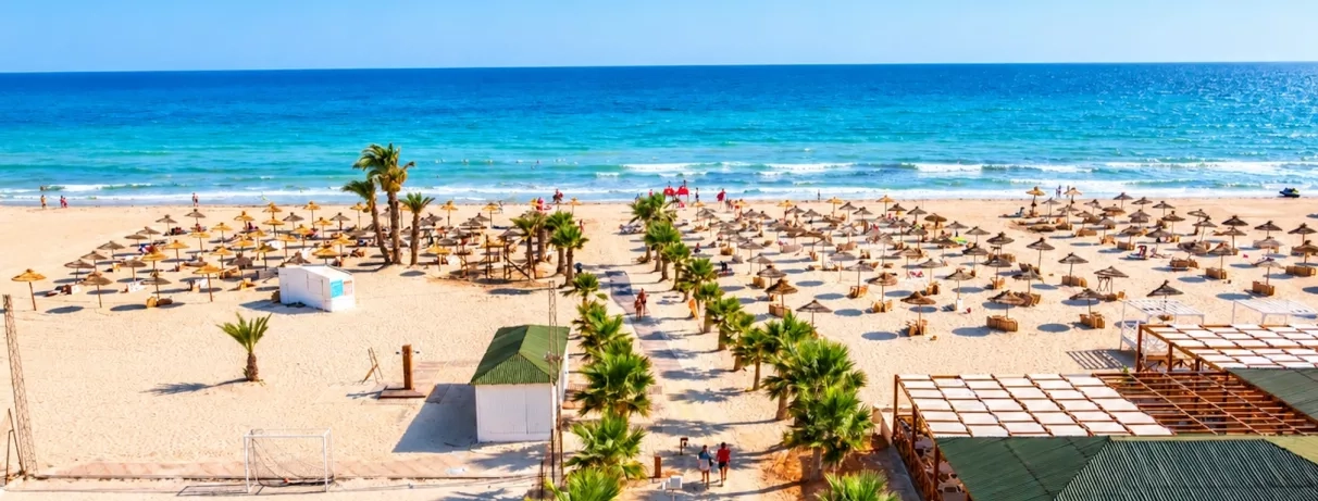 Une vaste étendue de sable blanc parsemée de parasols traditionnels, face à une mer turquoise.