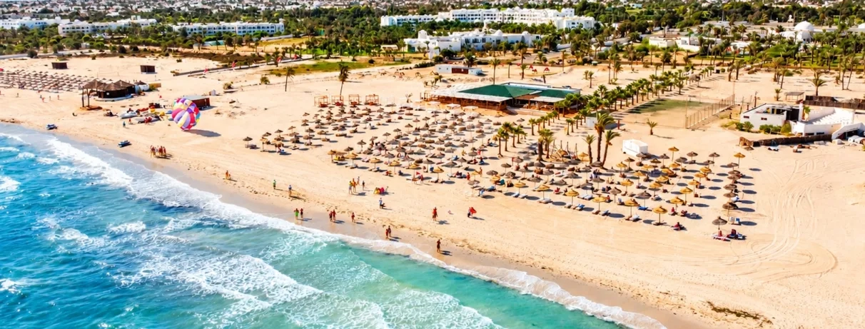 Une immense plage de sable fin bordée de parasols en paille, avec ses espaces dédiés aux sports nautiques.