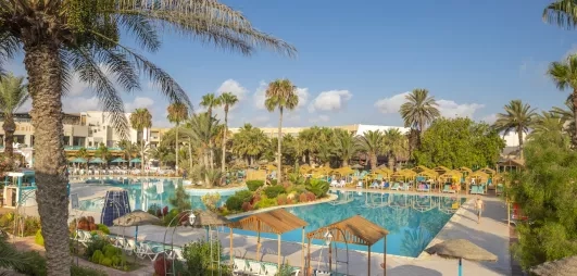 Grande piscine azur entourée de palmiers et paillotes au complexe hôtelier Welcome Meridiana à Djerba, Tunisie.