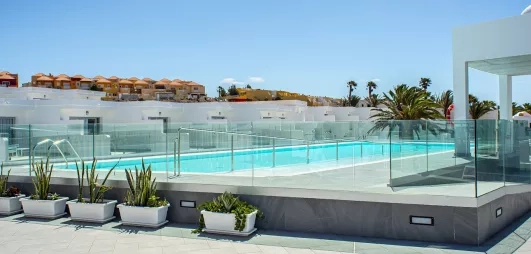 Une piscine aux eaux turquoise est entourée de rangées de plantes, sous un ciel bleu.
