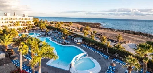 Un panorama ensoleillé montrant une piscine, nichée entre des bâtiments d'hôtel et la mer.