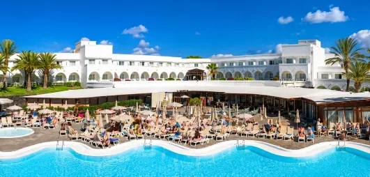 Une vue panoramique d'une grande piscine, bordée de transats devant l'hôtel.