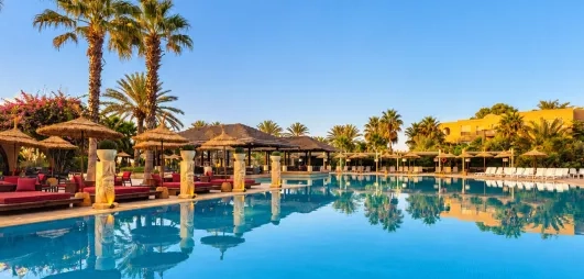Grande piscine entourée de palmiers, transats confortables et ambiance ensoleillée