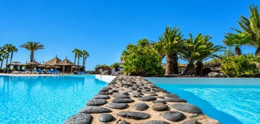 Un gros plan sur une séparation en pierre entre deux sections de la piscine, offrant une vue vers les jardins.