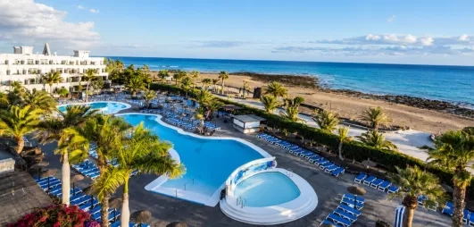 Un panorama ensoleillé montrant une piscine, nichée entre des bâtiments d'hôtel et la mer.